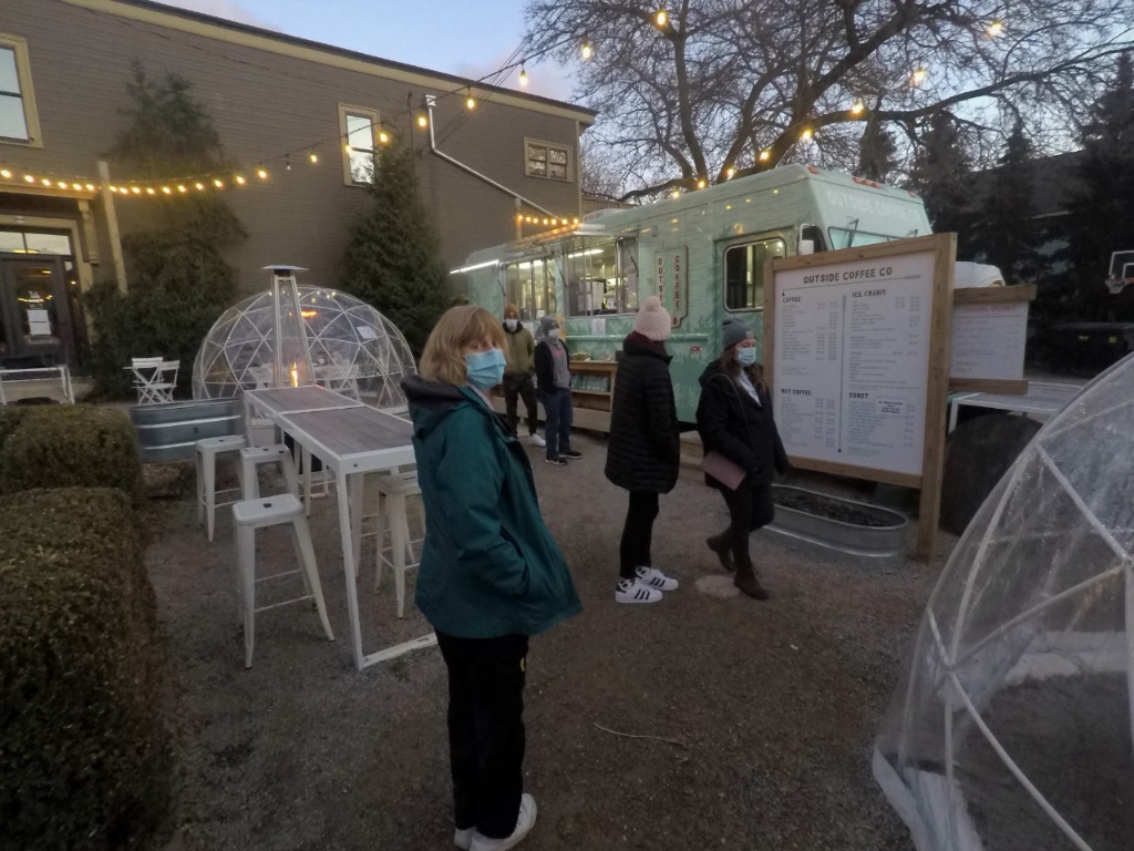 food truck in static position to serve hot and cold drinks in the chilly late December dusk in downtown Grand Rapids, Michigan: 2 persons study the menu board, 2 others place orders, one at the center foreground turns to the camera