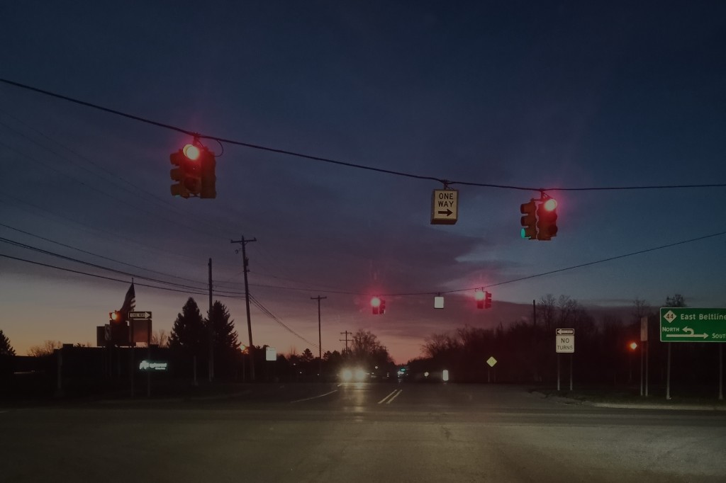 Background orange and purple of the dawn; foreground of 2 sets of 2 traffic lights displaying RED signal